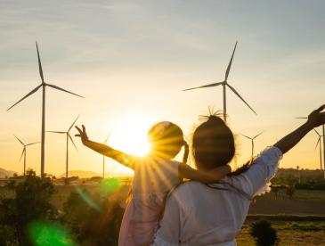 Woman and child with arms extended look at wind turbines as the sun sets